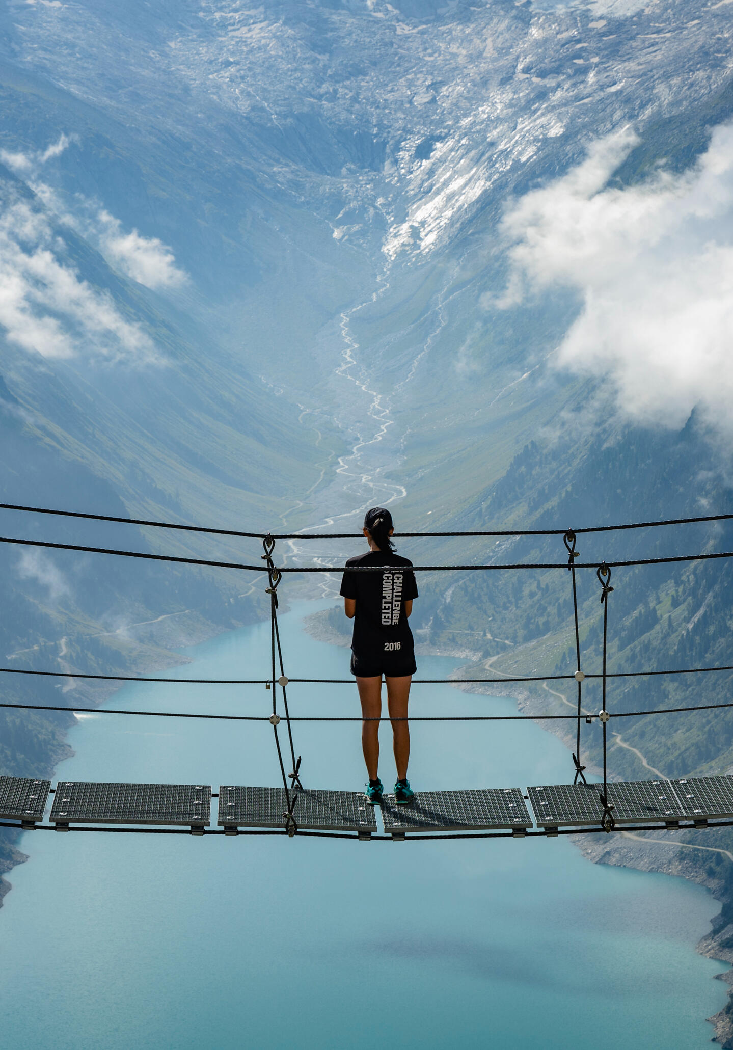 Girl standing on a hanging bridge above a big blue lake
