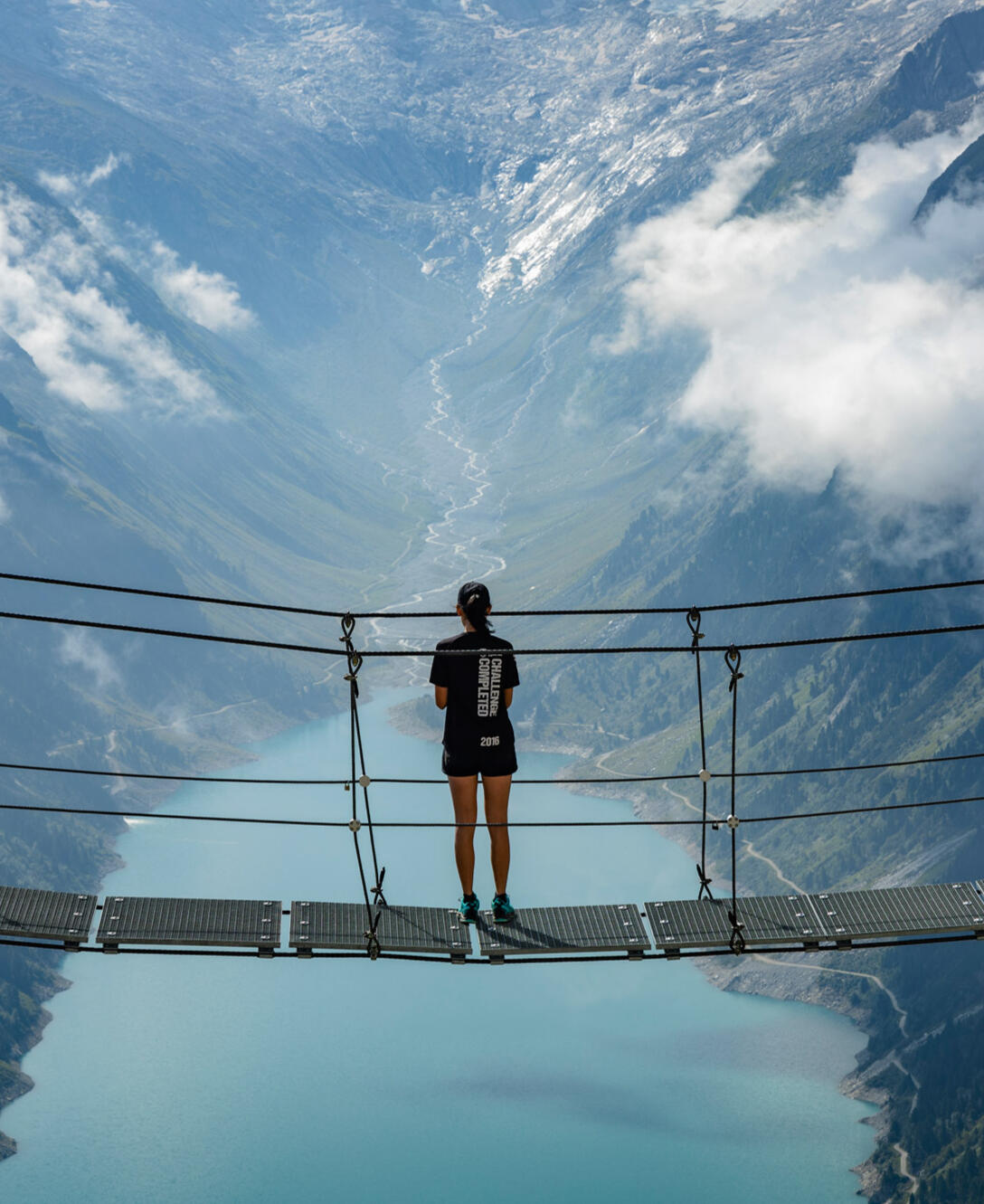 Abenteuer und Reisefotografie Girl standing on a hanging bridge above a big blue lake